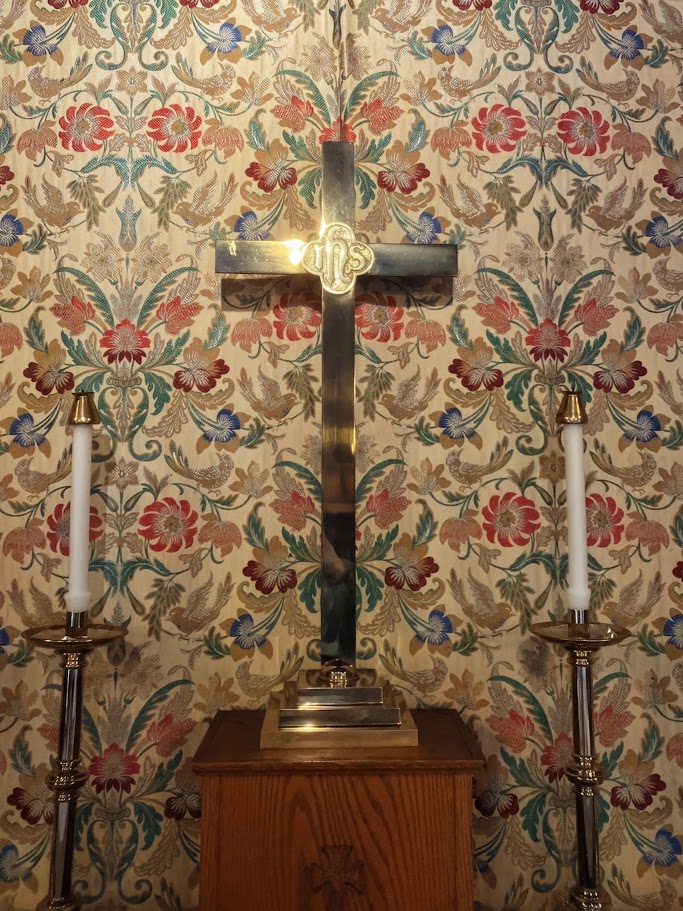 Brass altar cross between two lit candles against the patterned sanctuary wall