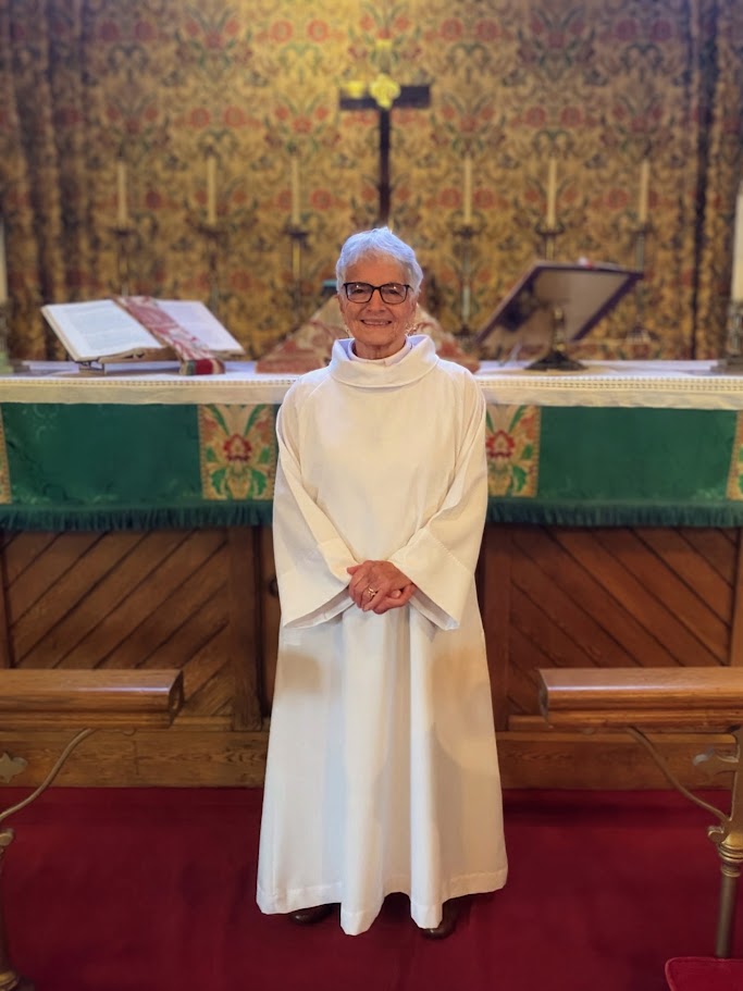 The Rev. Rebecca Harris standing in white vestments in the sanctuary of St. John's